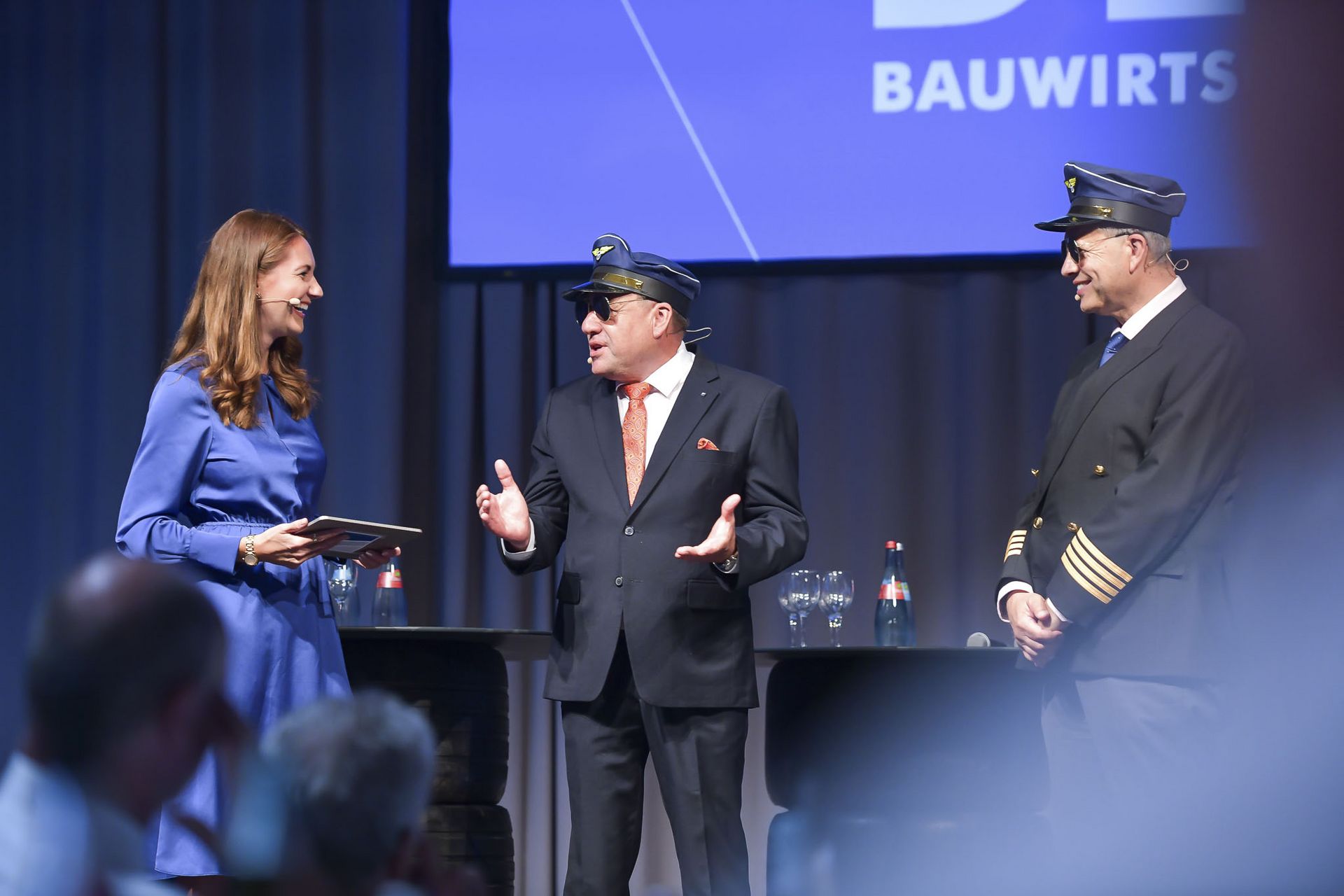 Tag der Bauwirtschaft 2025 Moderatorin Anja Lange begrüßt die pünktlich gelandeten "Verbandspiloten" Markus Böll und Thomas Möller.